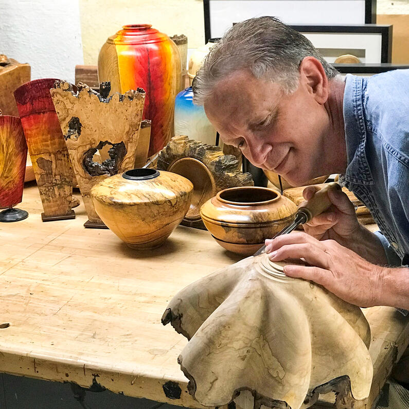 Carving a fluted wood bowl Artist carving flutes into a wood bowl, with many examples of fine art wood in background.